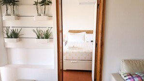 Een slaapkamer met een bed, nachtkastje, stoel en een plank met planten.