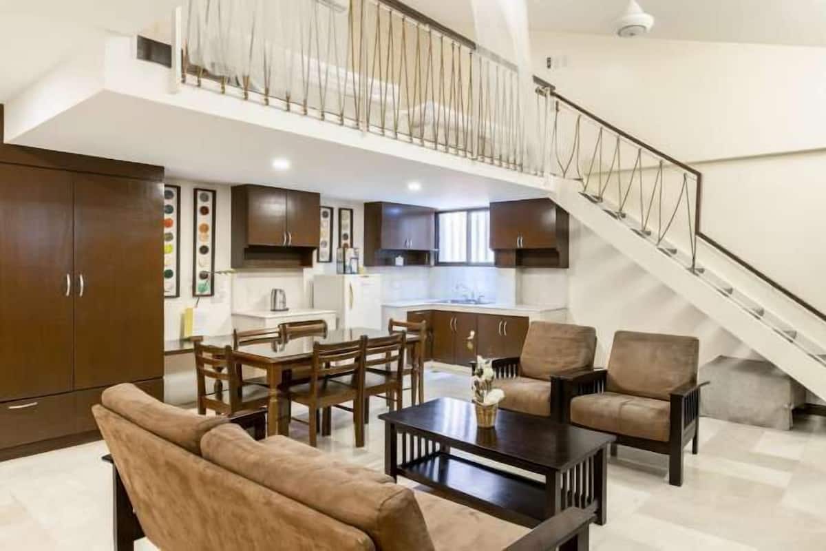 A spacious living area with a dining set, sofas, and a staircase leading to an upper level.