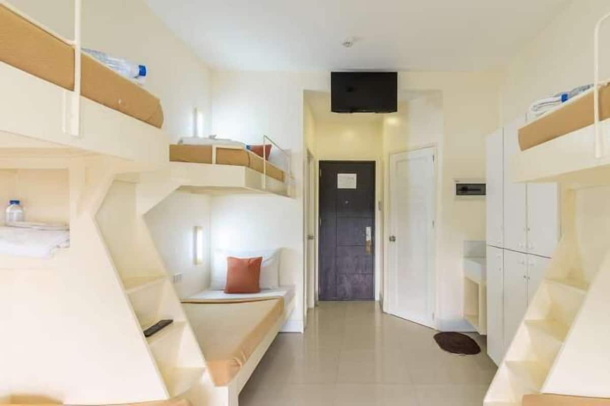 A corridor with bunk beds on either side, a door at the end, and a small shelf with items on the left side.