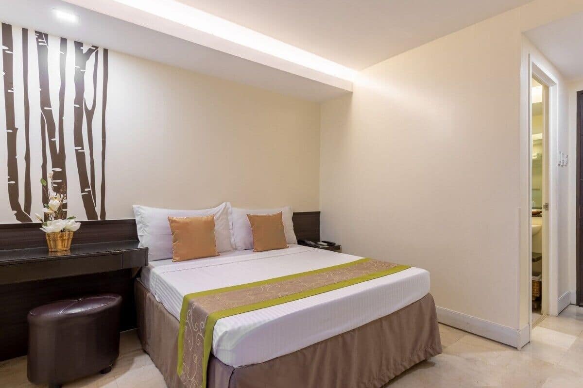 A hotel room with a bed, bedside table, and a dark wooden door.