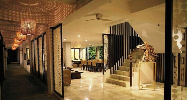 A modern hotel lobby with a staircase, a reception desk, and a dining area.