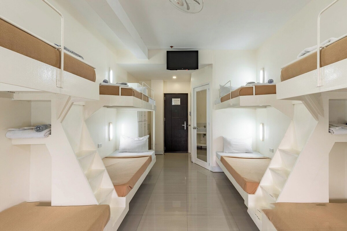 A corridor with bunk beds on either side, a door at the end, and a television mounted on the ceiling.
