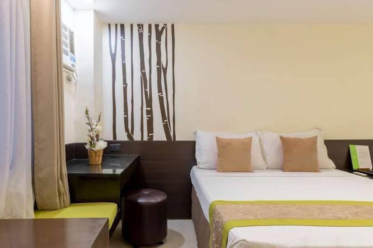 A hotel room with a bed, a desk, a chair, and a small table with a vase of flowers.