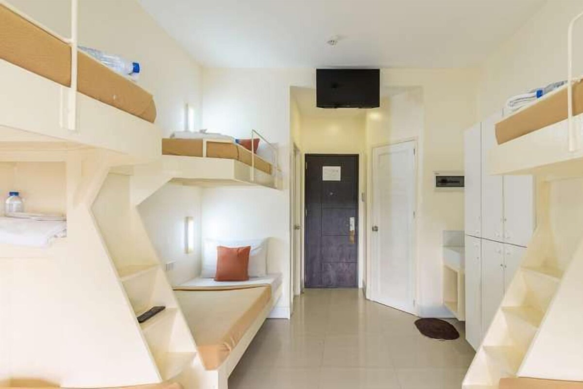 A corridor with bunk beds on either side, a door at the end, and a small shelf with items on the left side.