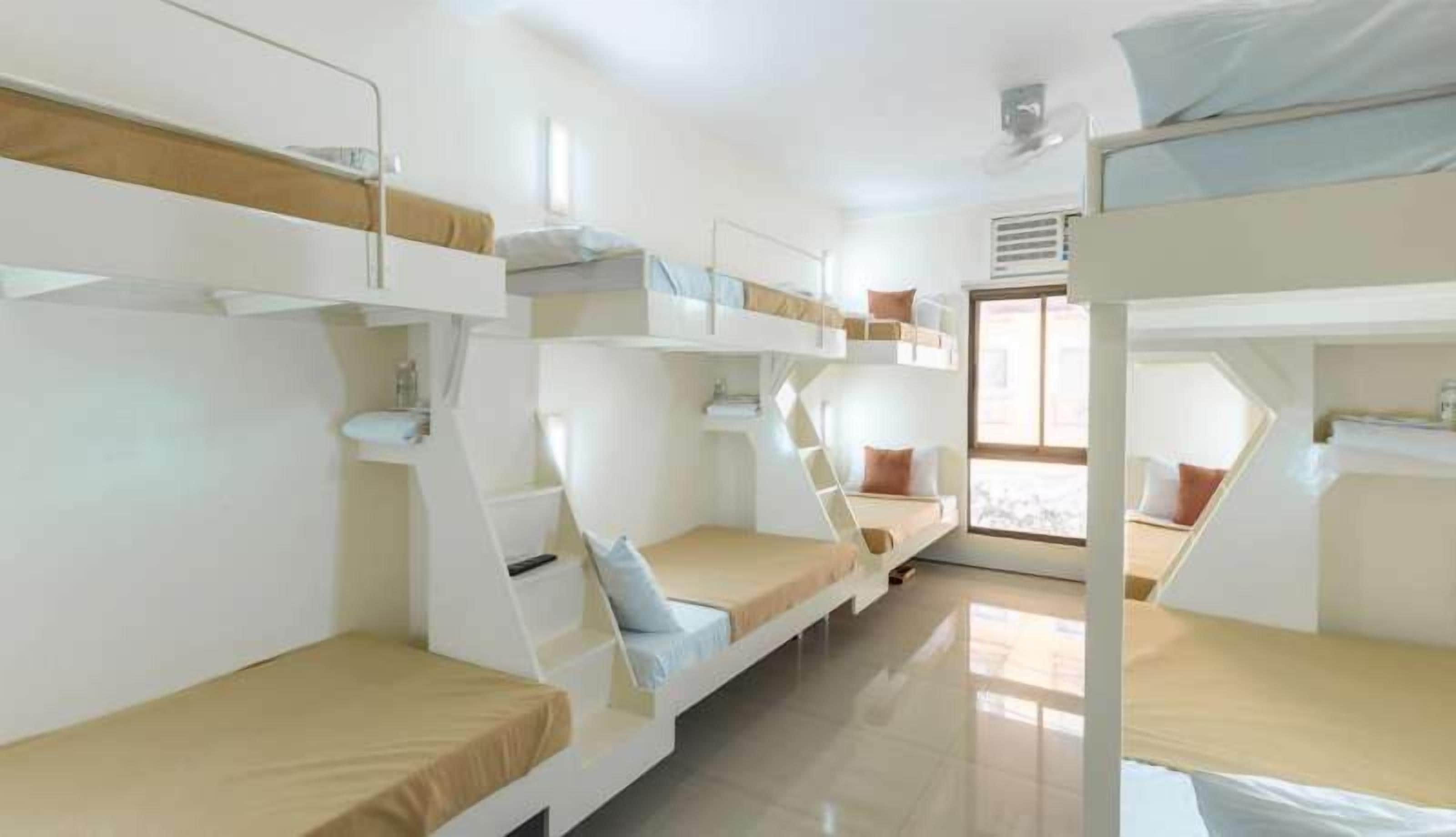 A dormitory-style room with bunk beds, a window, and a radiator.