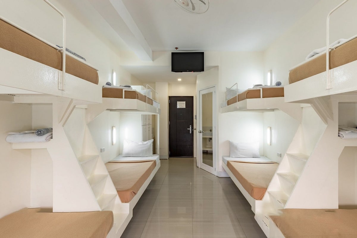 A corridor with bunk beds on either side, a door at the end, and a television mounted on the ceiling.