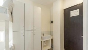 A bathroom with a white vanity, a dark wooden door, and a white cabinet. - Selah Garden Hotel Manila (Pasay)