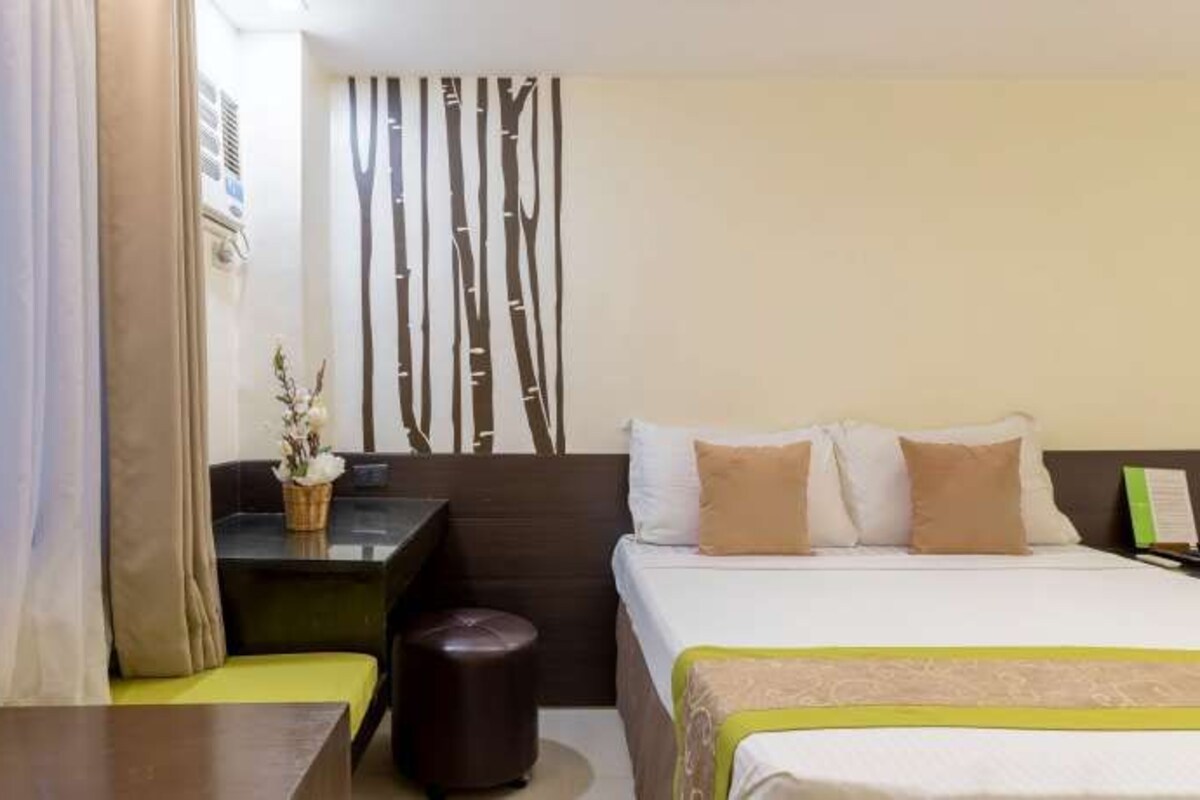 A hotel room with a bed, a desk, a chair, and a small table with a vase of flowers.