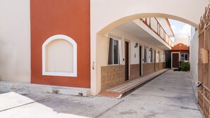 A corridor with a tiled floor, a red and beige building, and a gated area.