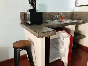 A compact kitchen with a microwave, coffee maker, sink, and a small refrigerator.