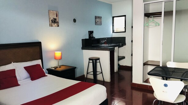 A hotel room with a bed, a desk with a sink, a chair, and a wardrobe.