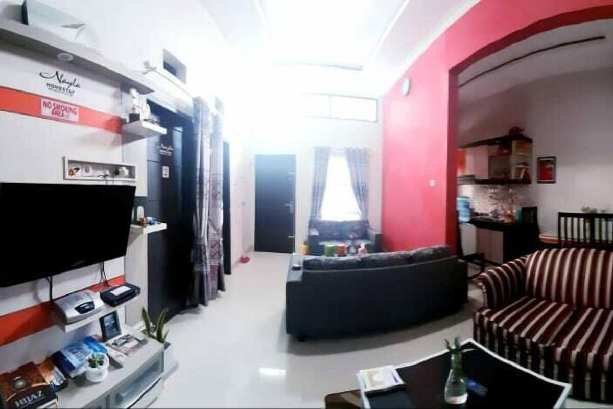 A living room with a sofa, a TV, and a coffee table. There is a red wall and a window with curtains.