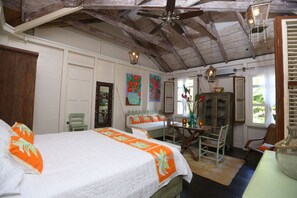 A bedroom with a bed, a desk, and a chair. There is a ceiling fan and a window with shutters.