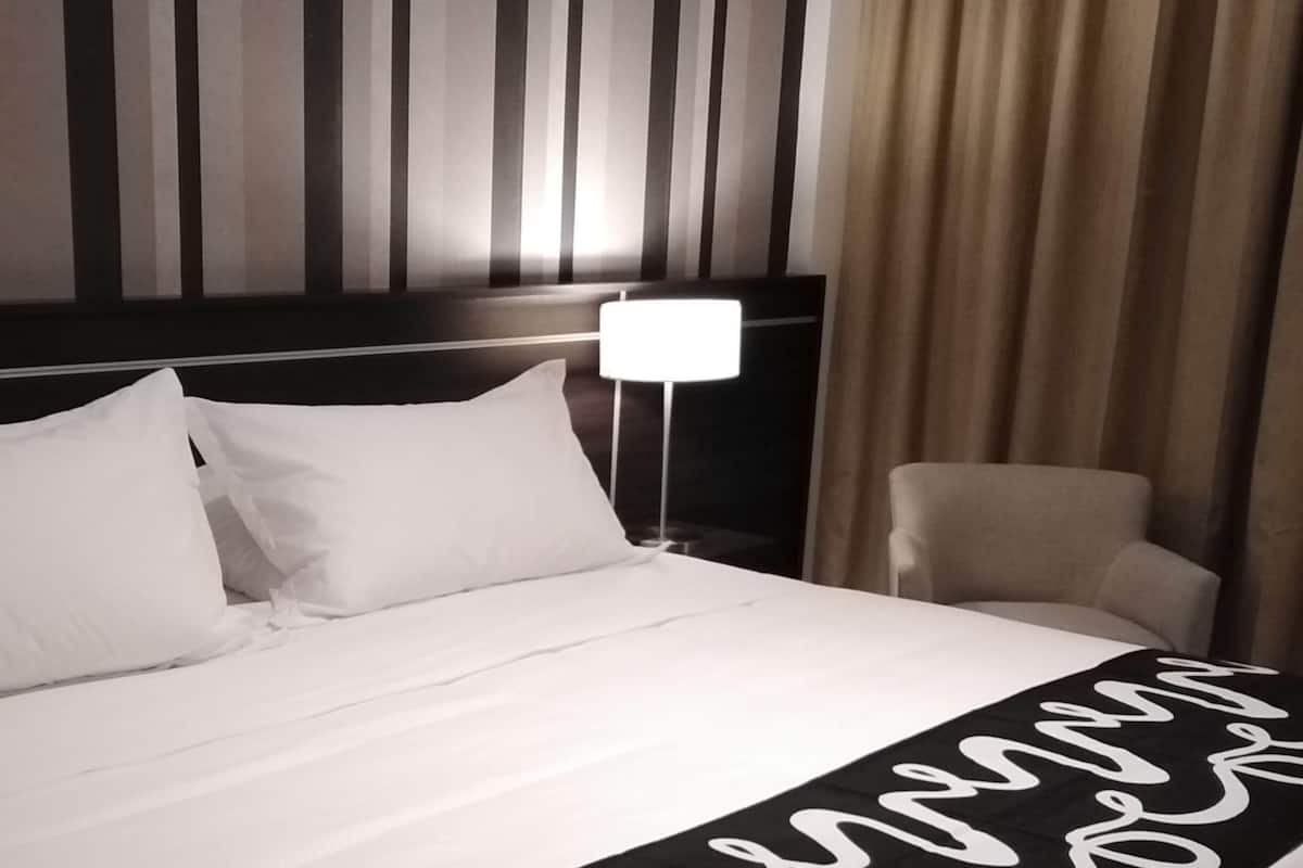 Ein Hotelzimmer mit einem großen Bett, einem Kopfteil mit vertikalen Streifen, einer Nachttischlampe und einem Sessel.