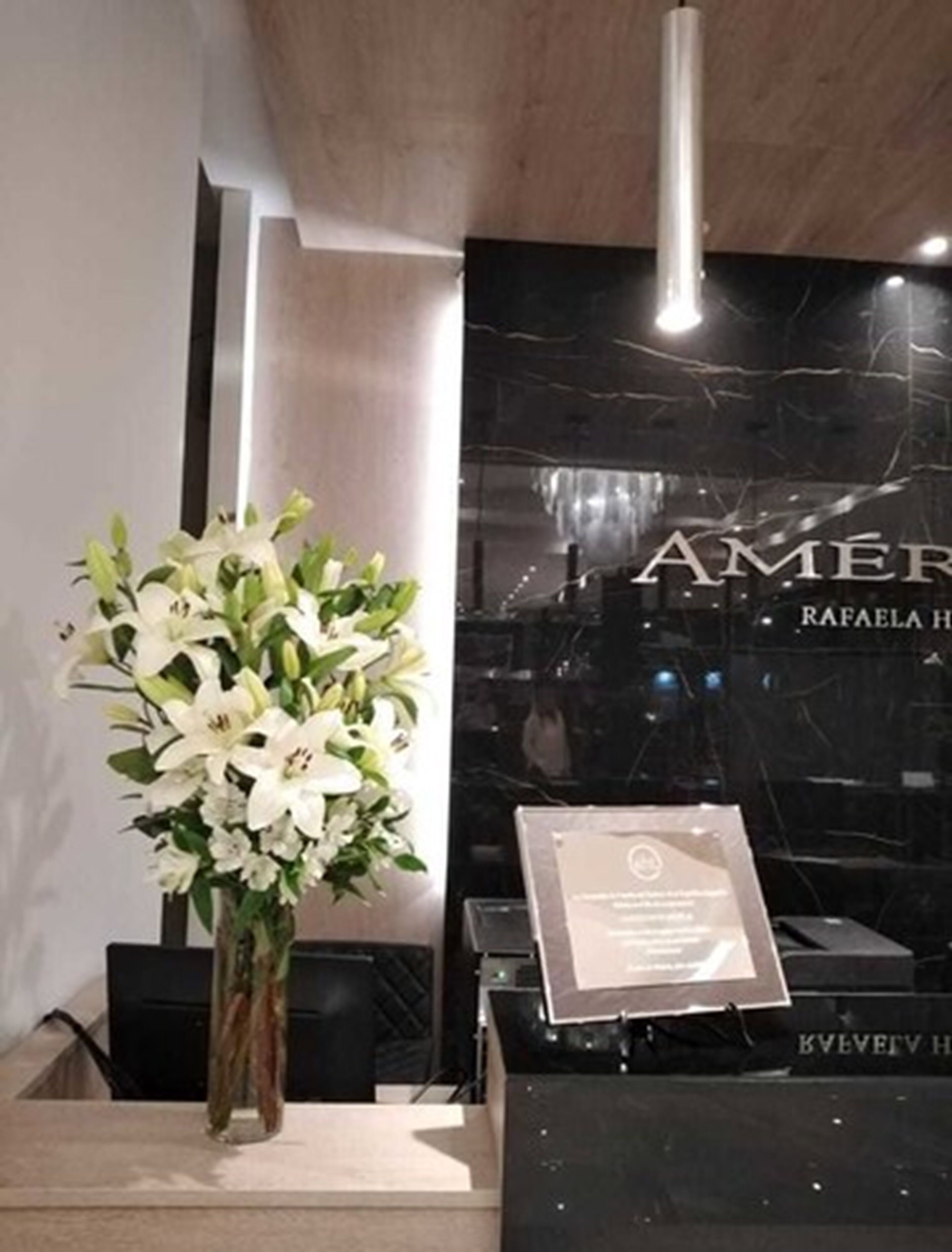 Un área de recepción con una pared de mármol negro, un arreglo floral blanco y un cartel con texto.