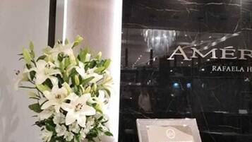 Un área de recepción con una pared de mármol negro, un arreglo floral blanco y un cartel con texto.