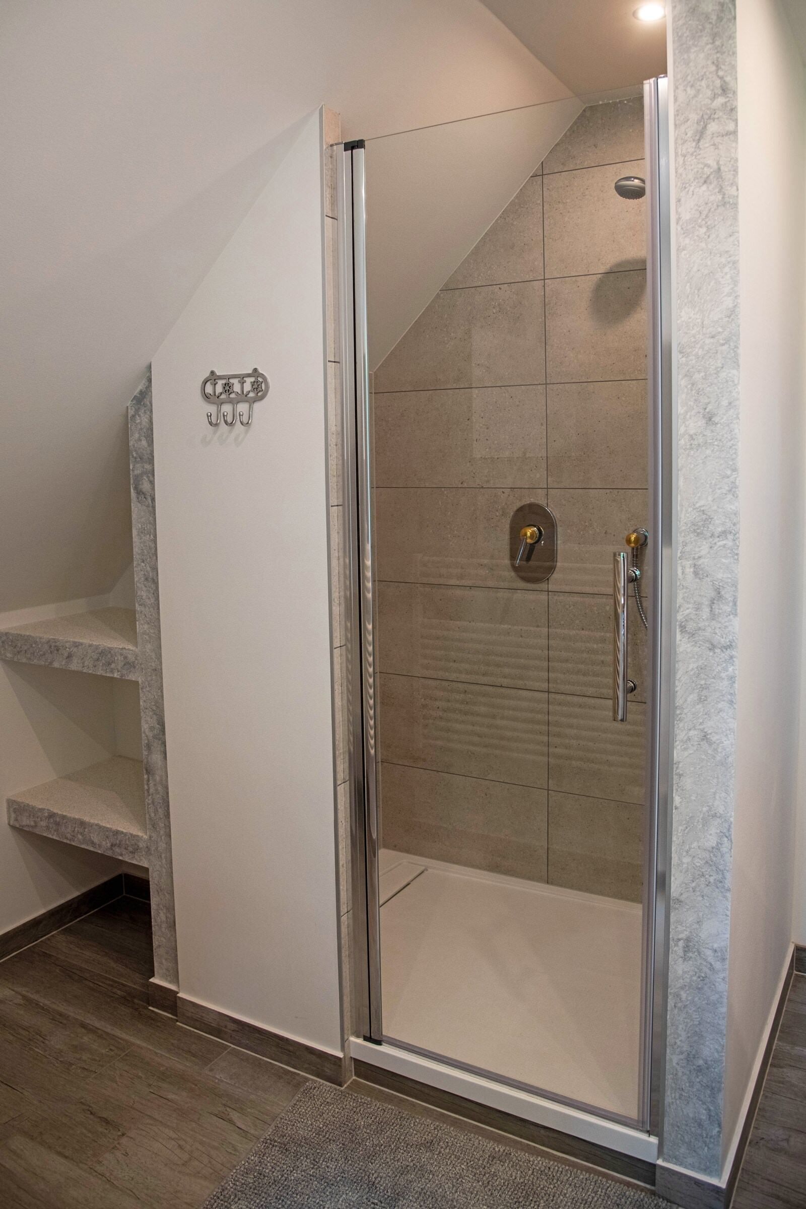 Une douche fermée par des parois en verre, avec un mur carrelé et une poignée en métal.