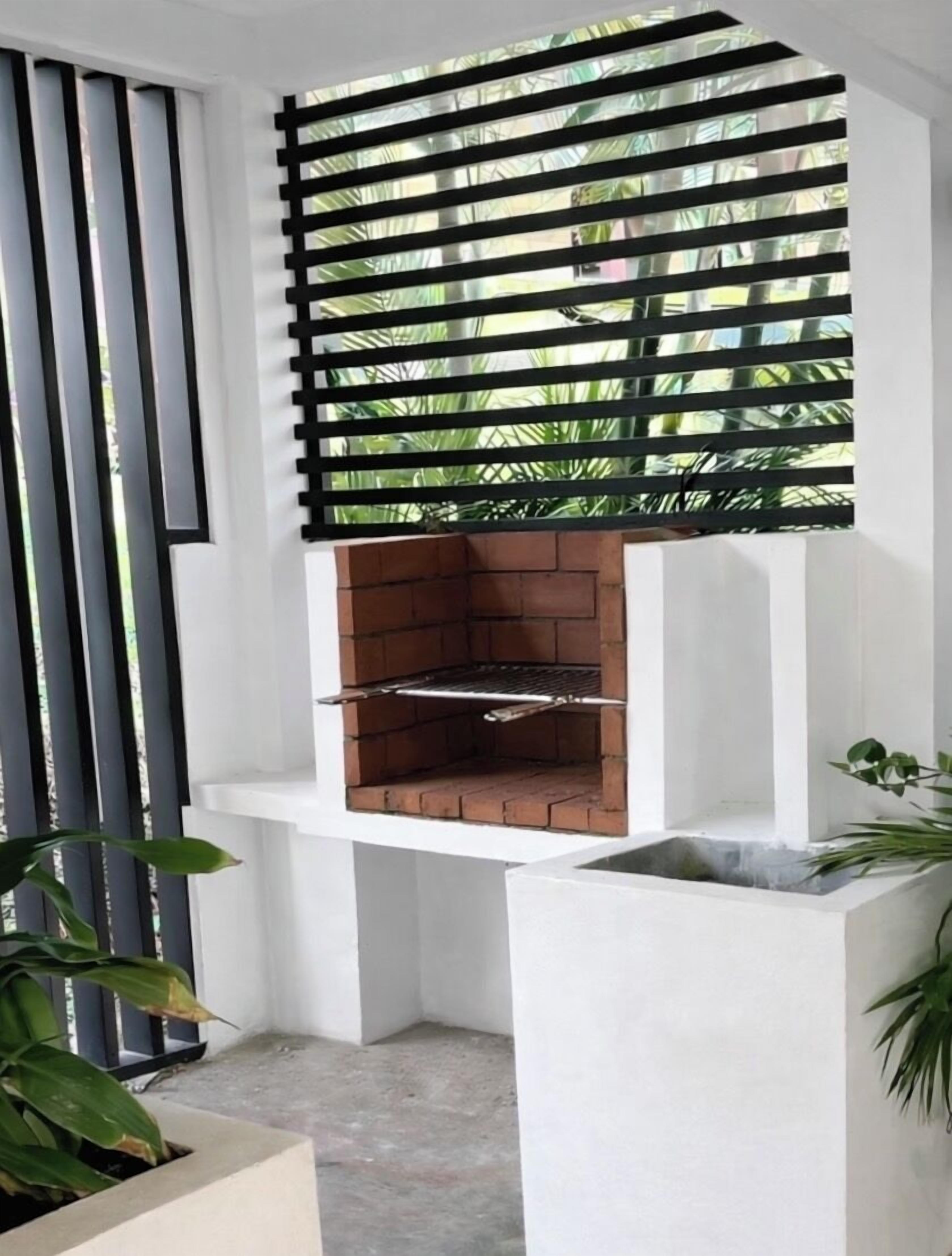 Un espace barbecue extérieur moderne, doté d’un four en briques, entouré de murs blancs et protégé par une grille en métal noir.