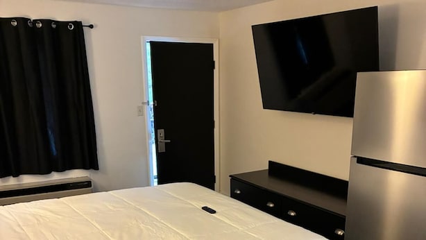 Hotellihuone, jossa on sänky, seinälle asennettu taulutelevisio, jääkaappi ja tummanvärinen lipasto.