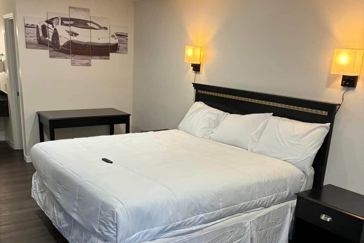 A neatly made bed with white linens, a dark headboard, and two bedside lamps.