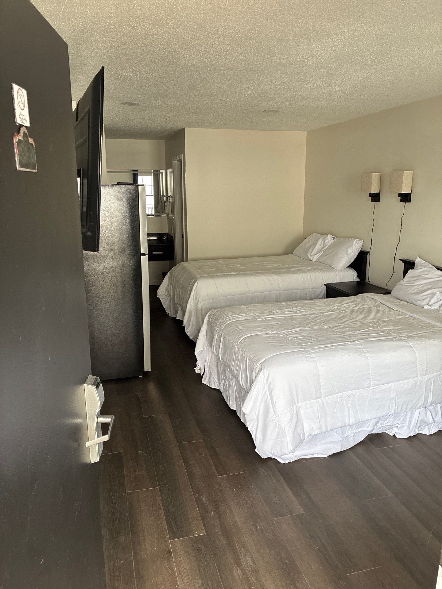 Een hotelkamer met twee bedden, een koelkast, een kleine kitchenette en een wandlamp.