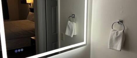 A modern bathroom with a large mirror, a round sink, and a towel rack.