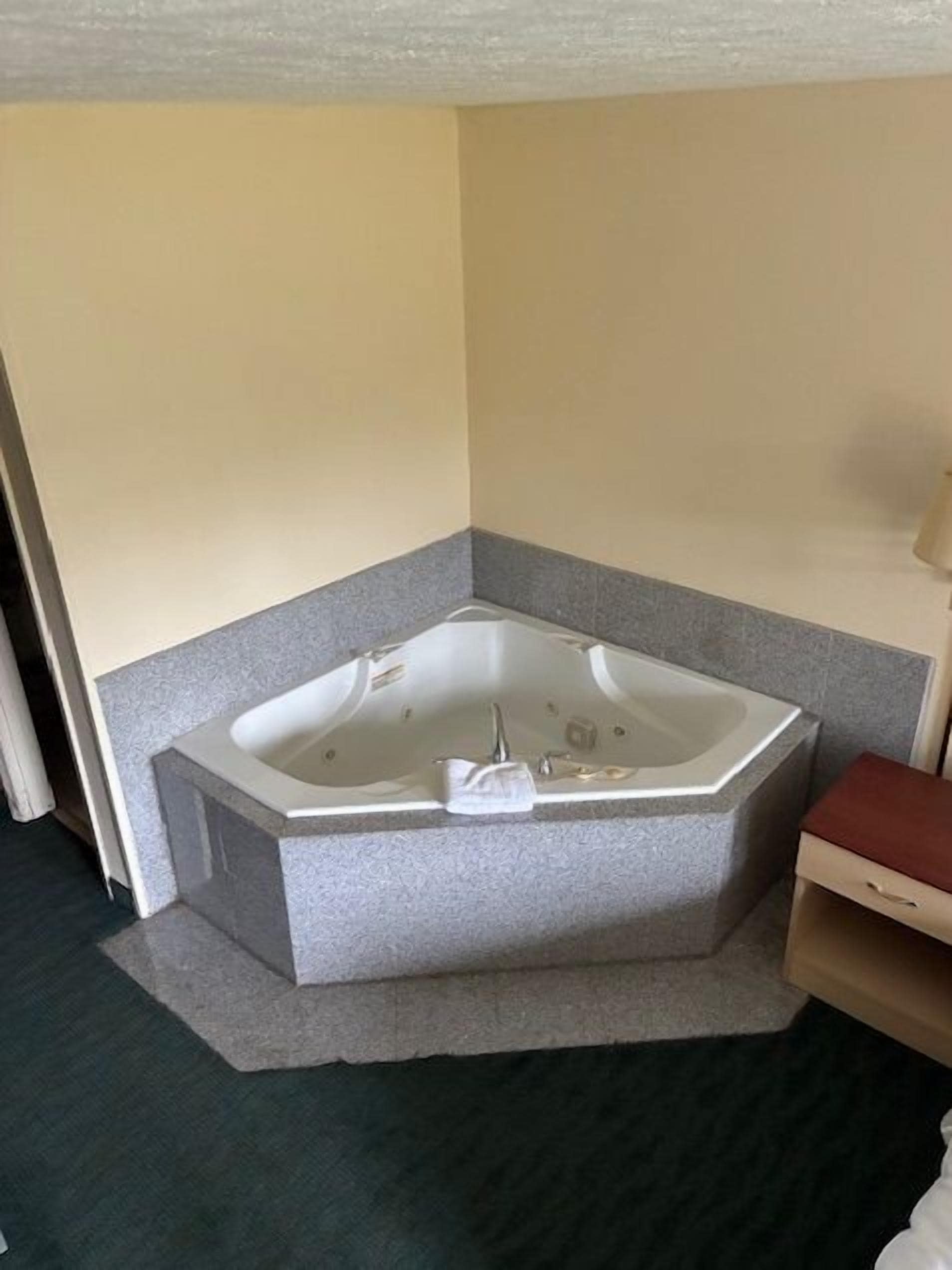 A corner bathroom with a freestanding bathtub, a small wooden bench, and a towel rack.