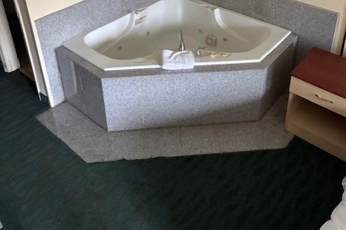 Ein Eckbadezimmer mit freistehender Badewanne, einer kleinen Holzbank und einem Handtuchhalter.
