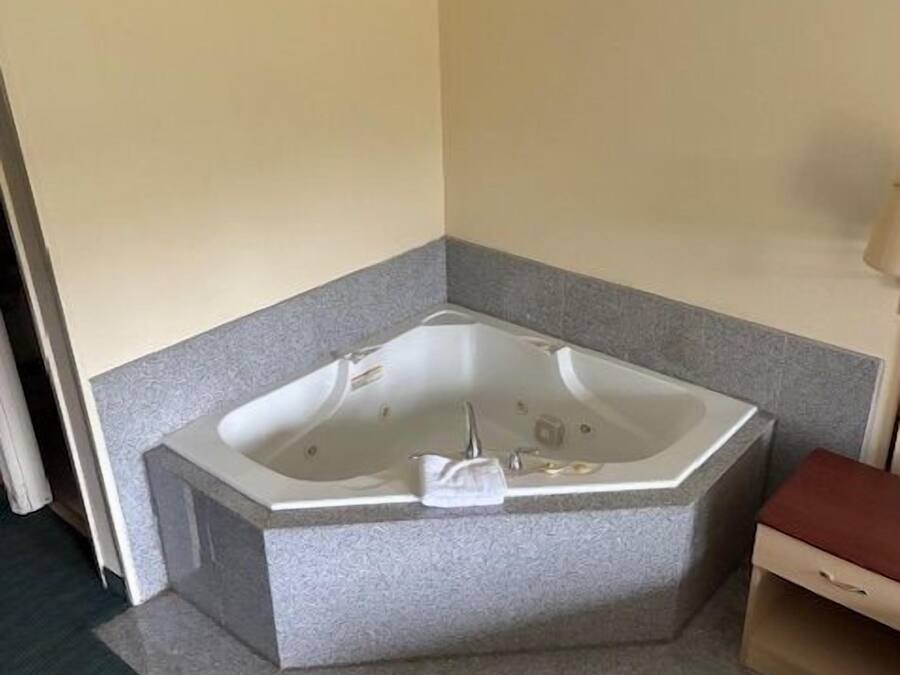 A corner bathroom with a freestanding bathtub, a small wooden bench, and a towel rack.