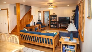 Un salon avec un escalier en bois, un canapé, un téléviseur et une bibliothèque.