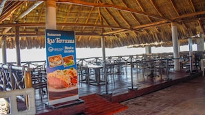 A restaurant with a thatched roof, outdoor seating, and a sign advertising seafood dishes.