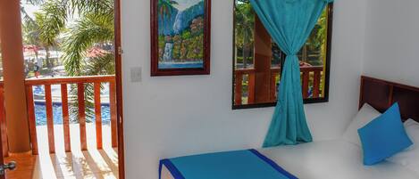 Un dormitorio con cama, ventana con vista a un balcón y un cuadro en la pared.