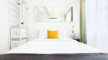 A hotel room with a bed, a nightstand, a mirror, a shelf with storage boxes, and a window with curtains.