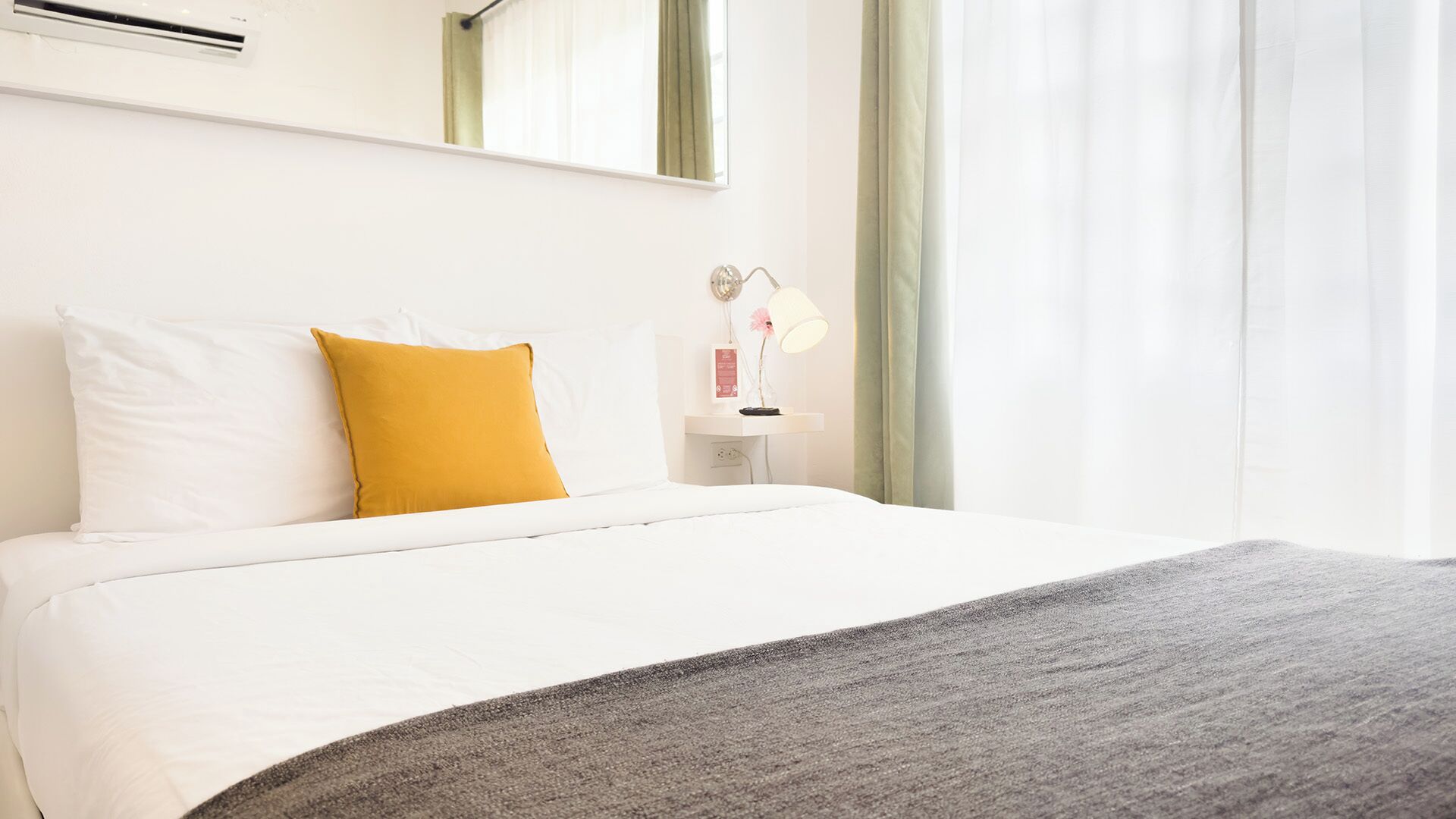 A hotel room with a bed, a nightstand, a lamp, and a window with curtains.