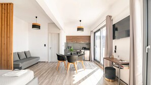 A modern living room with a sofa, dining table, and chairs, a kitchen in the background, and large windows with curtains. - Dreamy Athens Penthouse with Acropolis View (Athina)