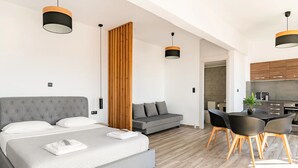 A modern hotel room with a large bed, a gray sofa, a dining area with a table and chairs, and a kitchen in the background. - Dreamy Athens Penthouse with Acropolis View (Athina)