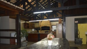 Uma cozinha rústica com forno de tijolos, vigas de madeira e um vaso de planta no balcão.