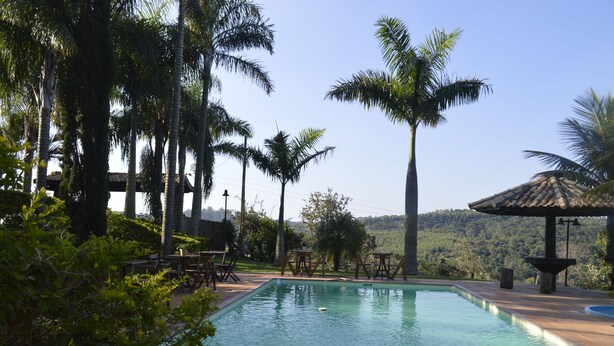 Piscina com palmeiras, móveis de exterior e montanhas ao fundo.