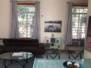 A living room with a sofa, a glass coffee table, a dining table with chairs, a white cabinet with decorative items, and large windows with curtains. - Gladiolas 1 209 (Ponce)