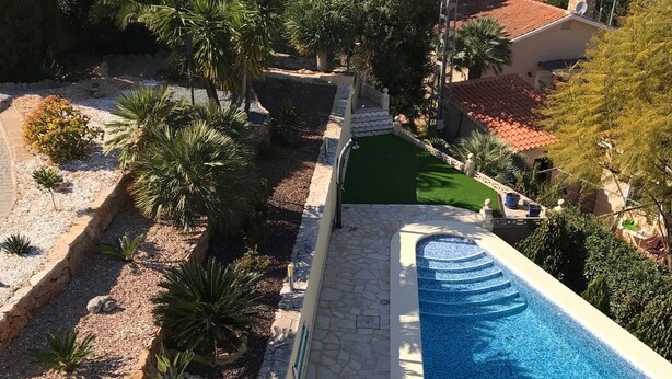 Ein Schwimmbecken mit einer Steindeck und einer kleinen Whirlpool-Anlage, umgeben von angelegten Grünflächen und Palmen.