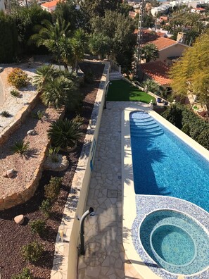 A swimming pool with a stone deck and a small hot tub, surrounded by landscaped greenery and palm trees. - Sunny apartment with salt water pool, whirlpool, mountain view (Dénia)