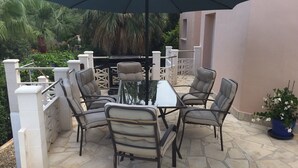 Eine Terrasse mit Tisch, vier Stühlen, Sonnenschirm und einem Blumentopf.