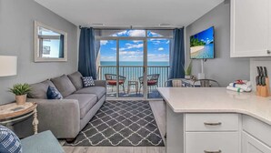 Un salon moderne comprenant un canapé, une table à manger et des chaises, un balcon avec vue et un coin cuisine équipé de placards et d’un téléviseur.