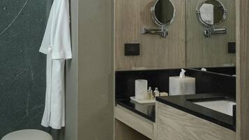 Un baño moderno con pared de mármol, tocador de madera, dos espejos redondos, encimera negra y toallero blanco.