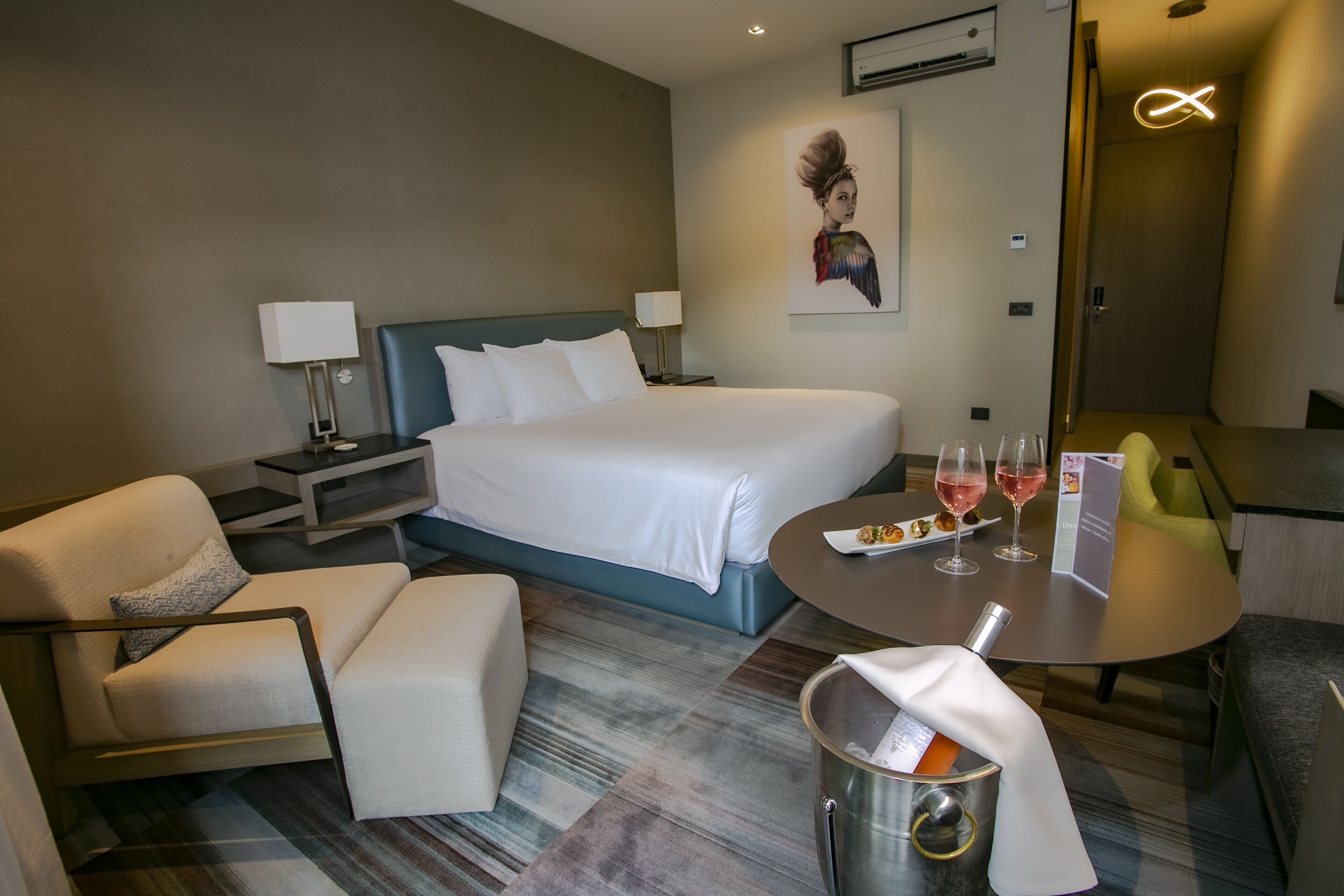 Une chambre d’hôtel comprenant un lit, un bureau, une chaise, une petite table avec des verres à vin et une poubelle.
