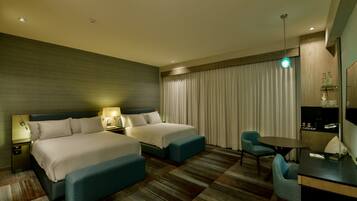 A hotel room with two beds, a desk, a chair, a small table, and a TV.