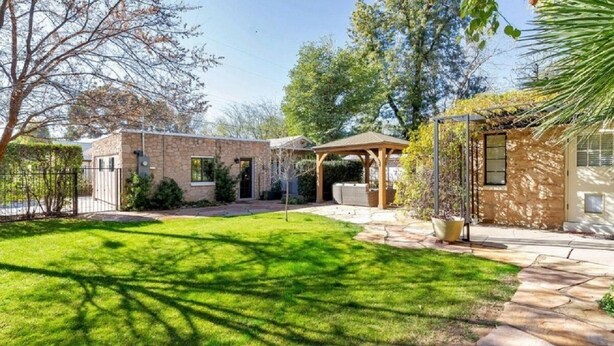 Ein gepflegter Garten mit einem Steinhaus, einer Holzpergola und einem Rasen.