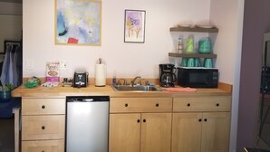 Eine kompakte Küche mit Geschirrspüler, Kaffeemaschine, Mikrowelle und einer Speisekammer mit Geschirr.