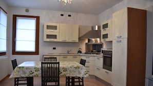 A modern kitchen with white cabinets, a dining table with chairs, and a built-in oven. - Your home near Venice - Free Parking (Venezia)