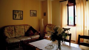 Una sala de estar con sofá, una silla, una mesa con un jarrón de flores y una ventana con cortinas.